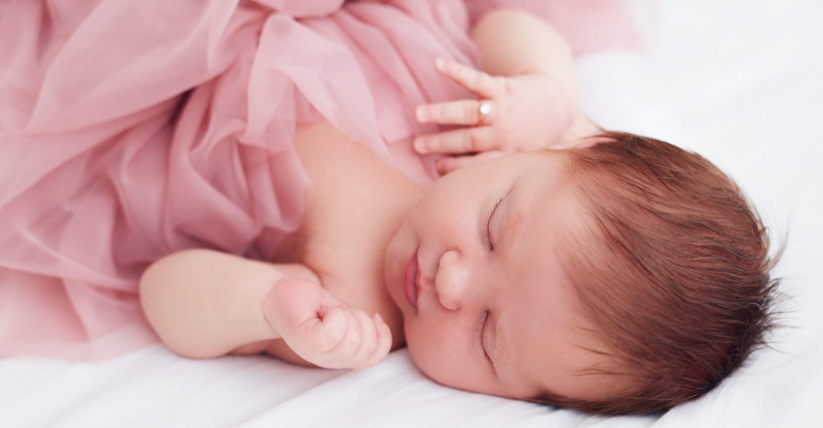 newborn, two weeks old baby girl in ruffle dress and with finger ring is sleeping peacefully